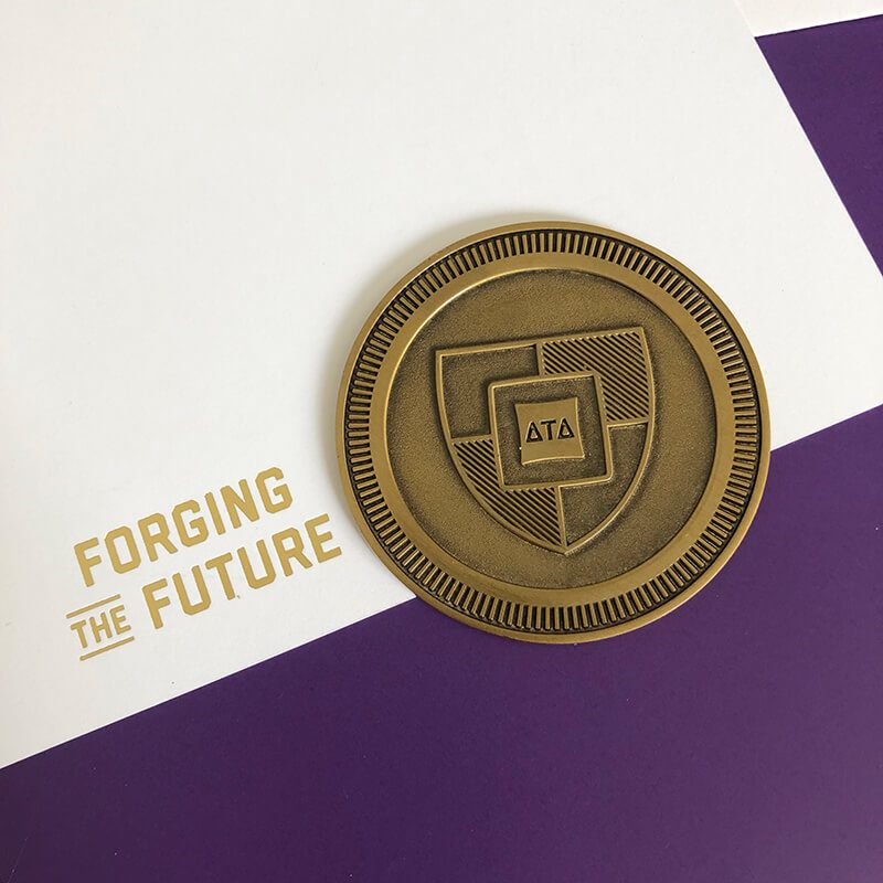 A coin with DTDF's new Forging the Future shield rests on a paper with the new logomark