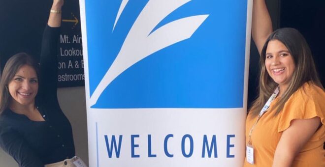 Lizzy and Lexi post next the FCA welcome sign at the Fraternity Communications Association's 2022 Seminar in Cincinnati, Ohio