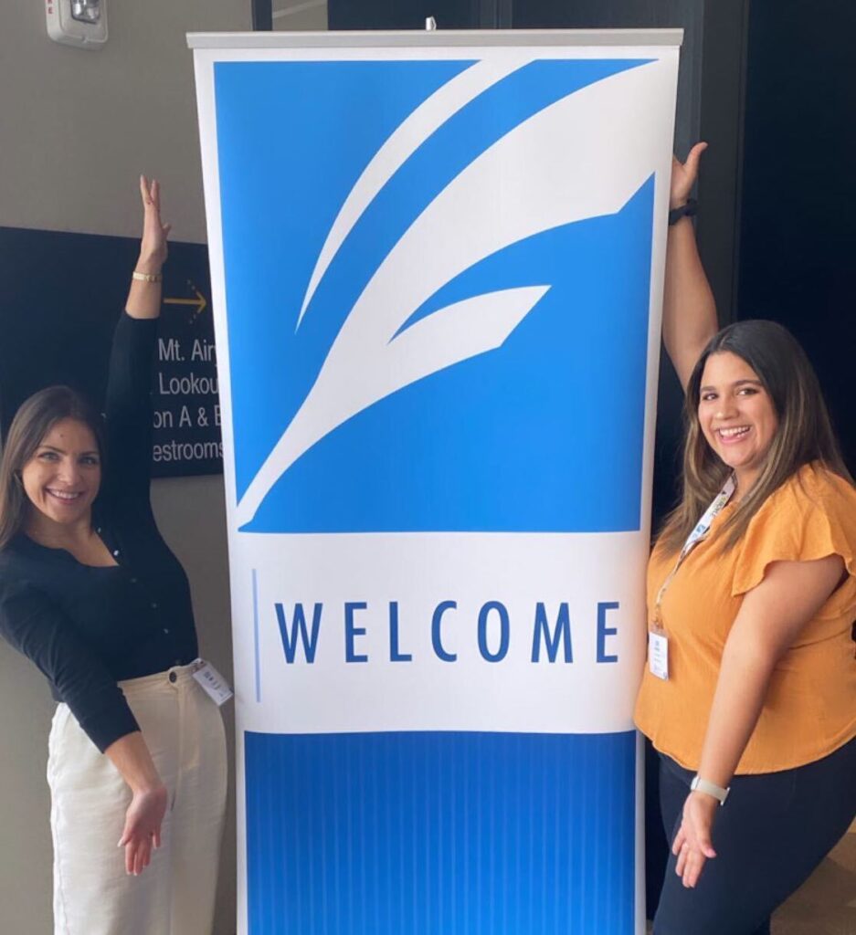 Lizzy and Lexi post next the FCA welcome sign at the Fraternity Communications Association's 2022 Seminar in Cincinnati, Ohio