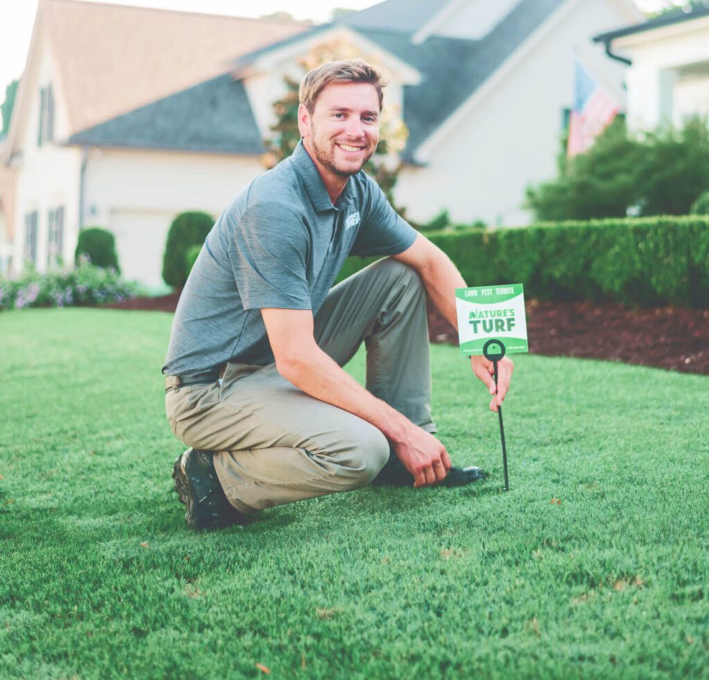 Man crouching on green grass with lawn sign