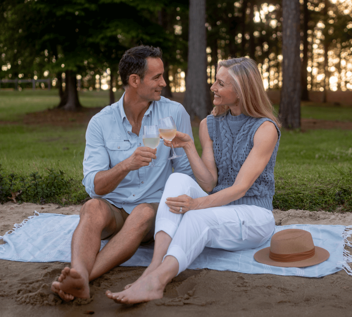 Photo of a man and a woman cheersing wine glasses at sunset on a sandy shore