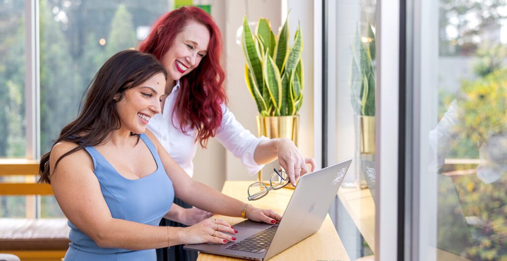 Two women gaze at a laptop, admiring their latest website update